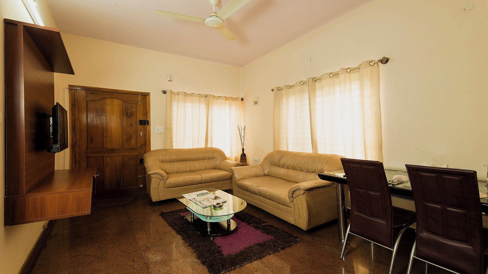 A living room with a sofa, a coffee table, a TV mounted on a wooden cabinet, and a ceiling fan.