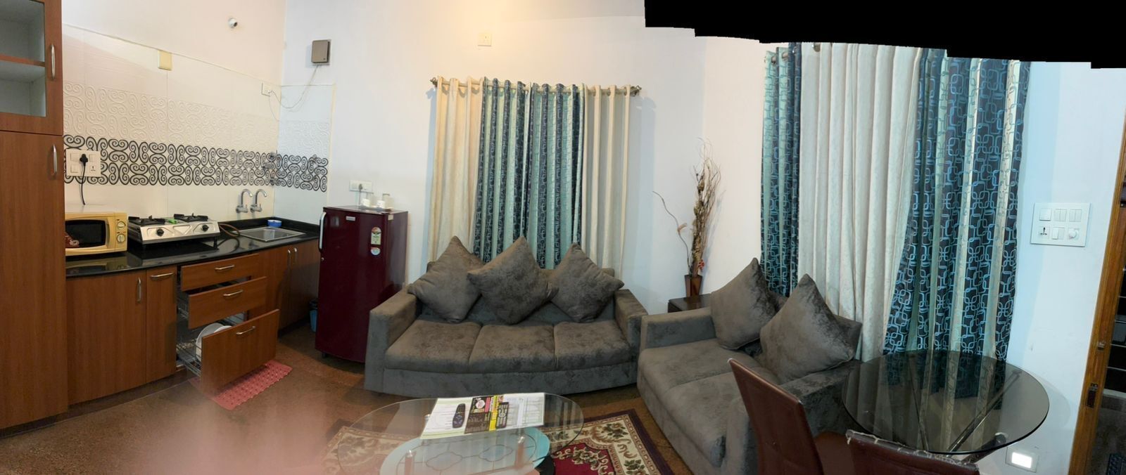 A compact living space with a kitchenette, two sofas, a glass coffee table, and curtains.