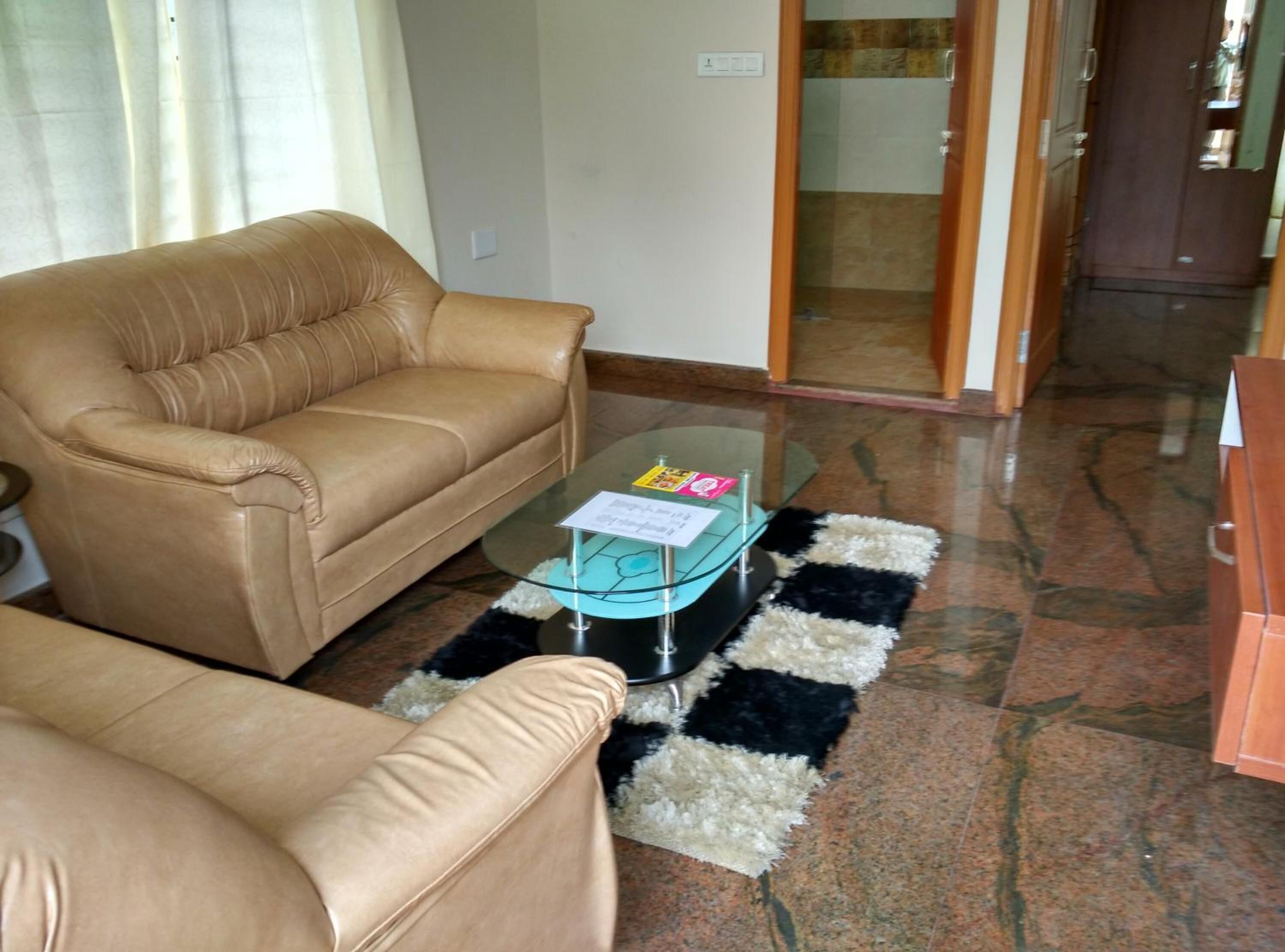 Una sala de estar con un sofá color beige, una mesa de centro de vidrio y un tapete blanco y negro.