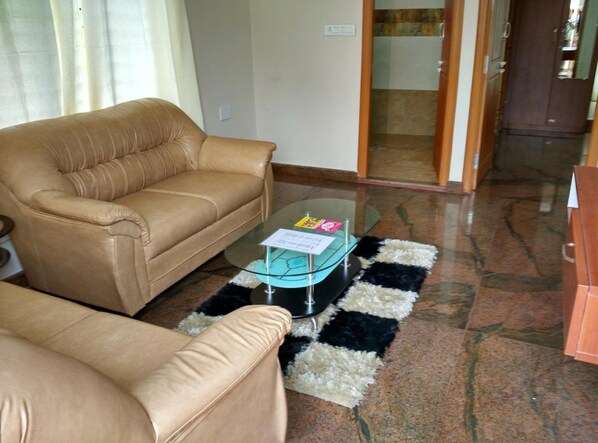A living room with a beige sofa, a glass coffee table, and a black and white rug.