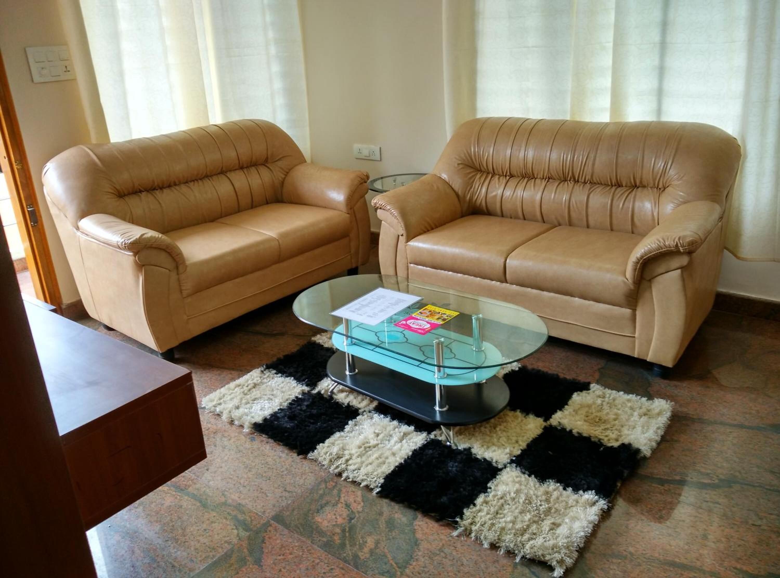 A living room with two beige leather sofas, a glass coffee table, and a black-and-white checkered rug.