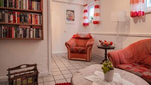 Un salon chaleureux avec une bibliothèque, un fauteuil rouge, un canapé et une table basse agrémentée d’une plante.