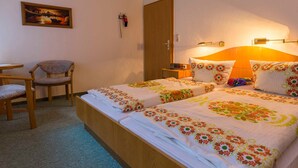 Une chambre d’hôtel avec deux lits, une chaise, une petite table et un tableau au mur.