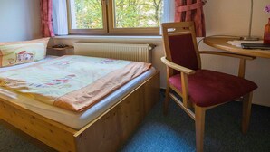 Un dormitorio con una cama de madera, un escritorio con silla, una ventana con cortinas y un radiador.