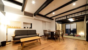 A living room with a sofa, dining table, chairs, and a wooden floor. - Machiya Kamo River 7 (Kyoto)