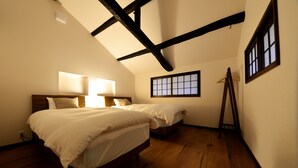 A bedroom with two beds, wooden flooring, a sloped ceiling with exposed beams, and a window with a view. - Machiya Kamo River 7 (Kyoto)