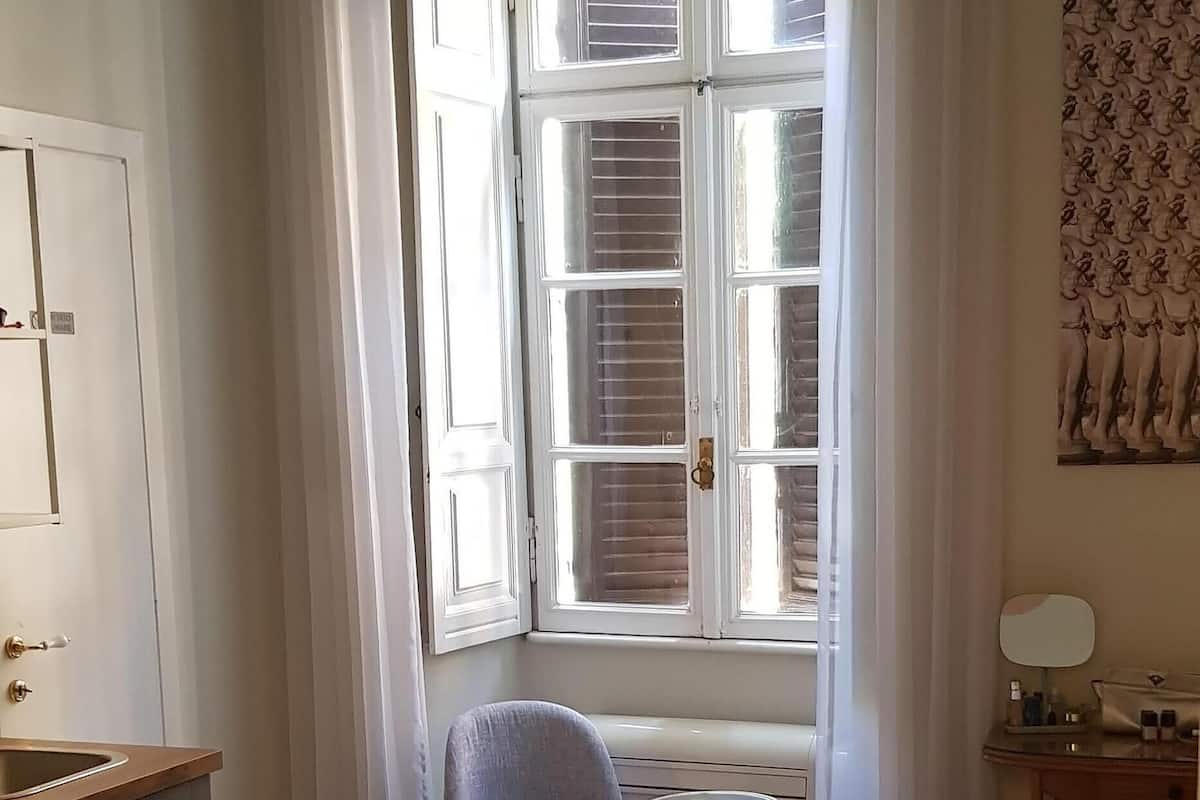Une chambre d’hôtel avec un lit, une chaise, une petite table, un bureau et une fenêtre avec des rideaux.