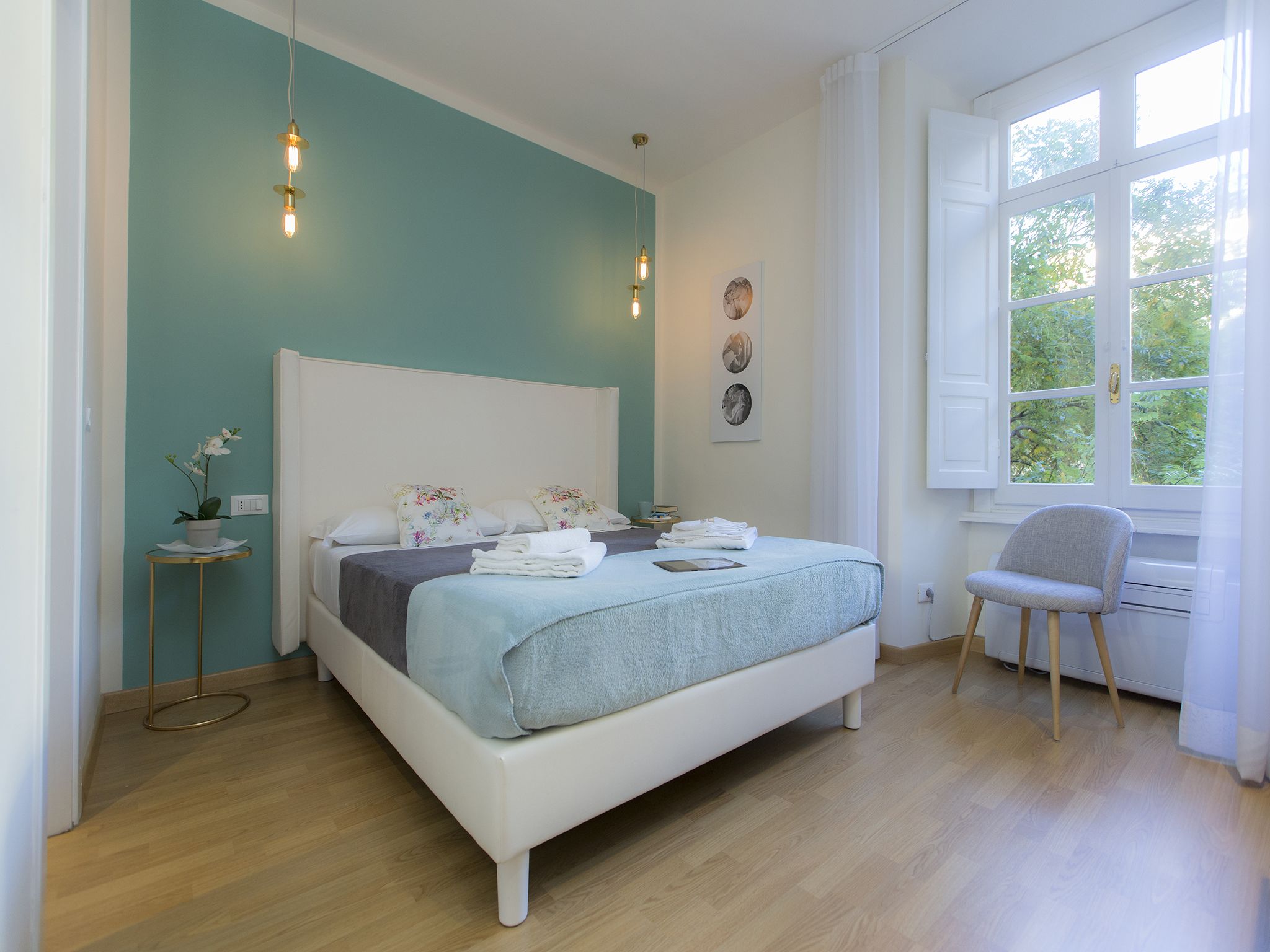 A bedroom with a bed, a chair, a window, and a small table with a plant.