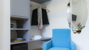 A modern room with a blue armchair, a wardrobe with shelves, a mirror, and a small table with a vase.