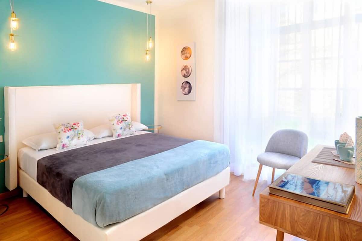 Une chambre bien rangée, avec un lit, une chaise, une table et une fenêtre avec des rideaux.