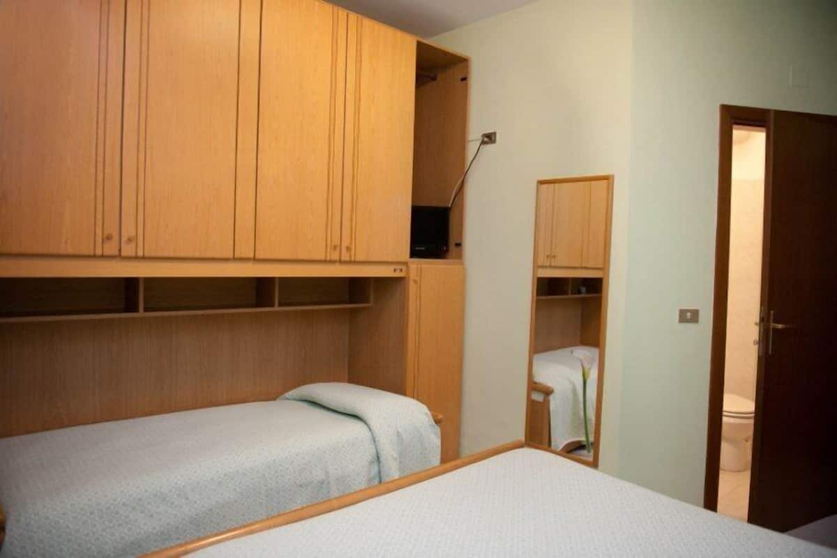 A small, compact room with two single beds, wooden cabinets, and a small bathroom.