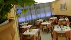 A dining area with tables set for two, featuring white tablecloths and orange chair covers. - Hotel Centrale (Loreto)