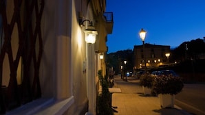 A street at dusk with buildings, street lamps, and parked cars. - Hotel Centrale (Loreto)