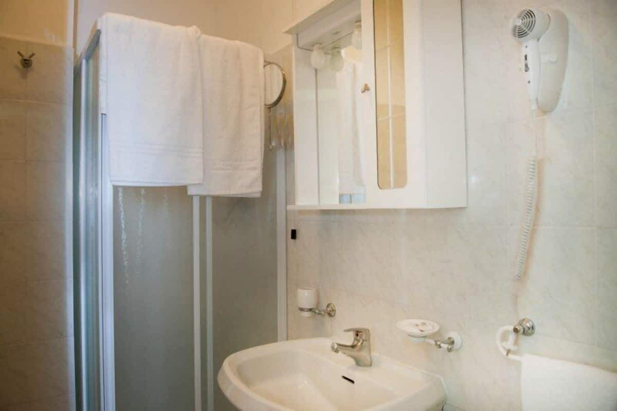 A bathroom with a shower, a sink, a mirror, and a hairdryer mounted on the wall.