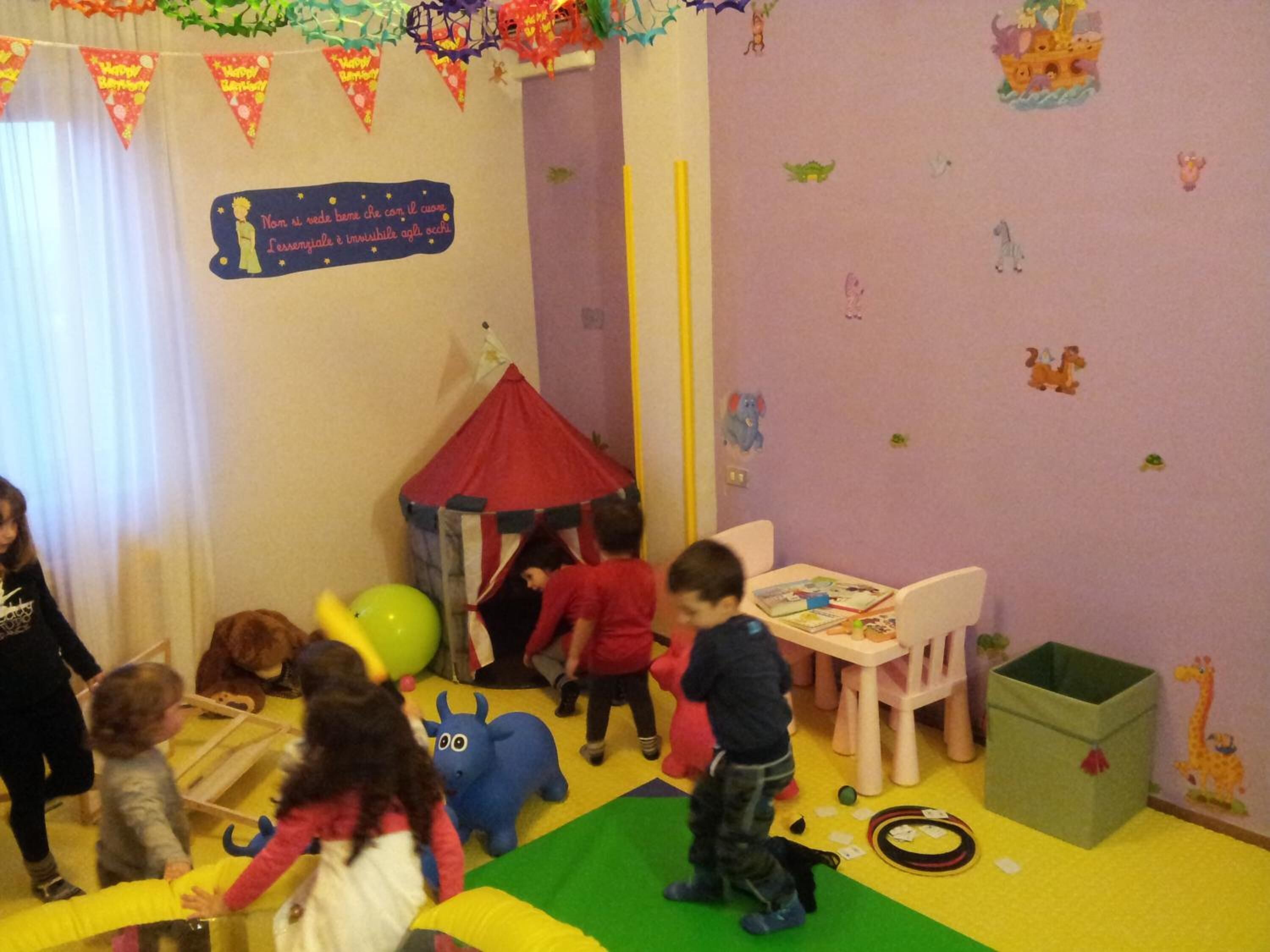 Una sala giochi per bambini con una tenda da gioco rossa, un tavolo pieno di giocattoli e un contenitore verde.