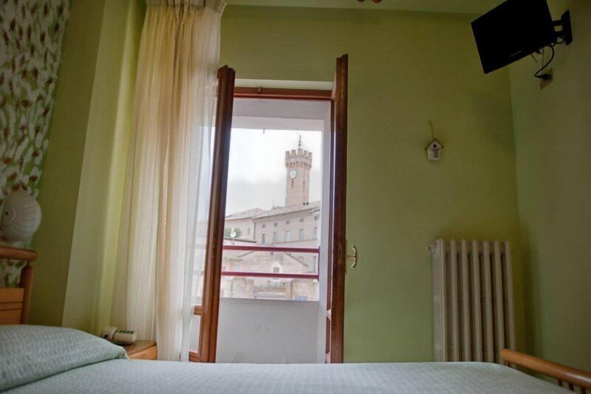 A room with a bed, a window with curtains, a radiator, and a view of a tower.