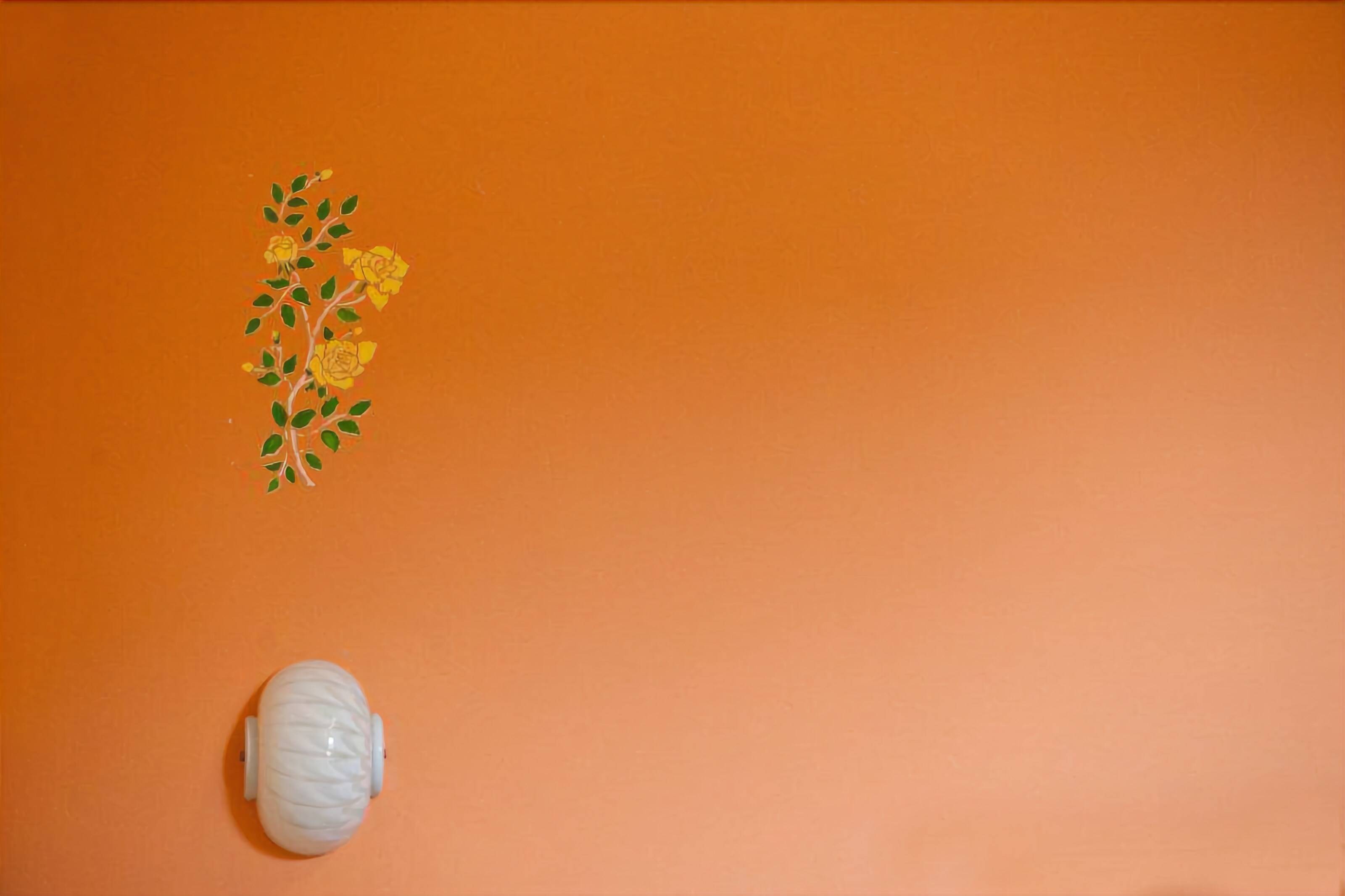 A plain orange wall with a white vase and a floral decal.