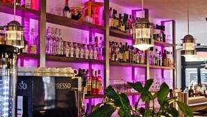 Zona de bar amb prestatges plens de botelles i gots, una màquina de cafè i llums penjants.