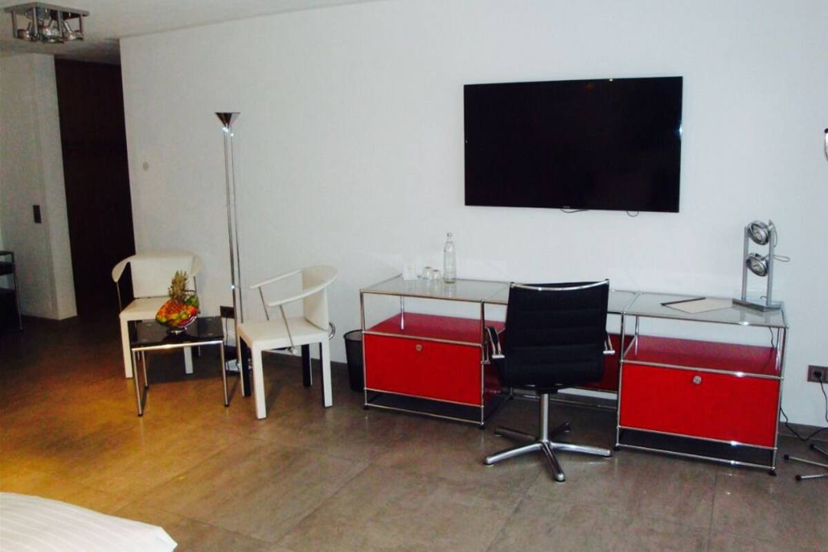 A modern hotel room with a bed, a desk with a chair, a flat-screen TV, and a floor lamp.