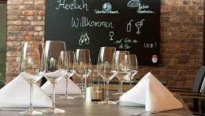 Interior de restaurant amb una pissarra que mostra frases i símbols alemanys, i diversos vasos de vi buits sobre la taula.