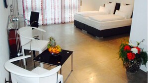 Habitació d'hotel amb un llit, un escriptori amb una cadira, una taula petita amb un plat de fruita i un vas amb flors.