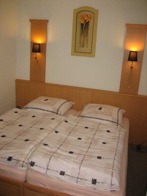 Una cama doble con una colcha a cuadros, dos lámparas de pared y una obra de arte floral enmarcada sobre la cama.