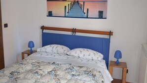 Un dormitorio con cama, un cuadro de un atardecer sobre un muelle y dos lámparas de noche.