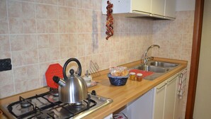 Una cocina con estufa a gas, hervidor, pileta y diversos utensilios de cocina sobre la encimera.