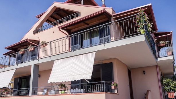 Un edificio residencial de varios pisos con balcones, ventanas amplias y plantas en macetas.