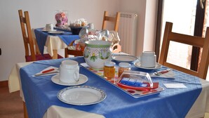Una mesa de comedor dispuesta con platos, tazas, una tetera y una bandeja con alimentos.
