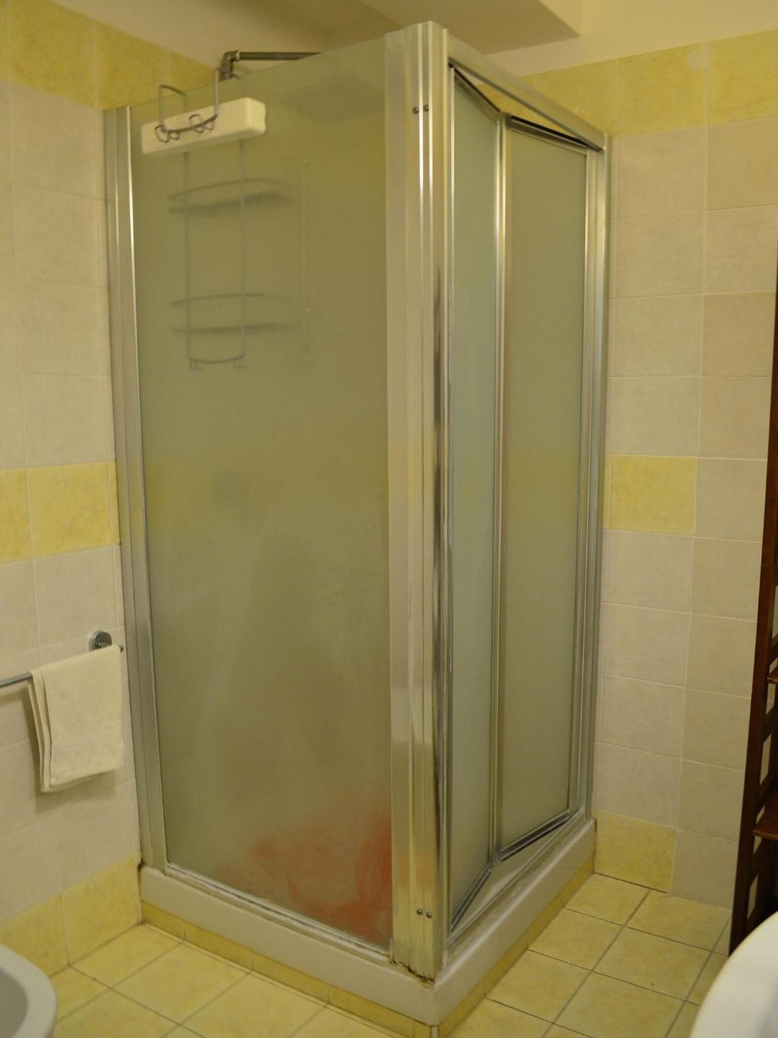 Un bagno con doccia vetrata, un water e pareti piastrellate di giallo.