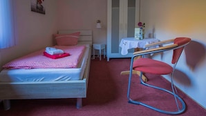 Un dormitorio con cama, una silla, un armario, una mesita con un jarrón y una puerta.