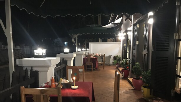 Un patio al aire libre con mesas y sillas, plantas en macetas y una barandilla.