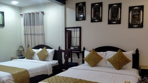 Habitación de hotel con dos camas, una mesita de noche con lámpara, un espejo y cuadros colgados en la pared.