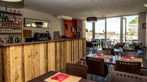 A restaurant with wooden walls, a bar area with various bottles, and outdoor seating with a view. - St Jean Luz Hotel Erromardie Suite 4p (Saint-Jean-de-Luz)