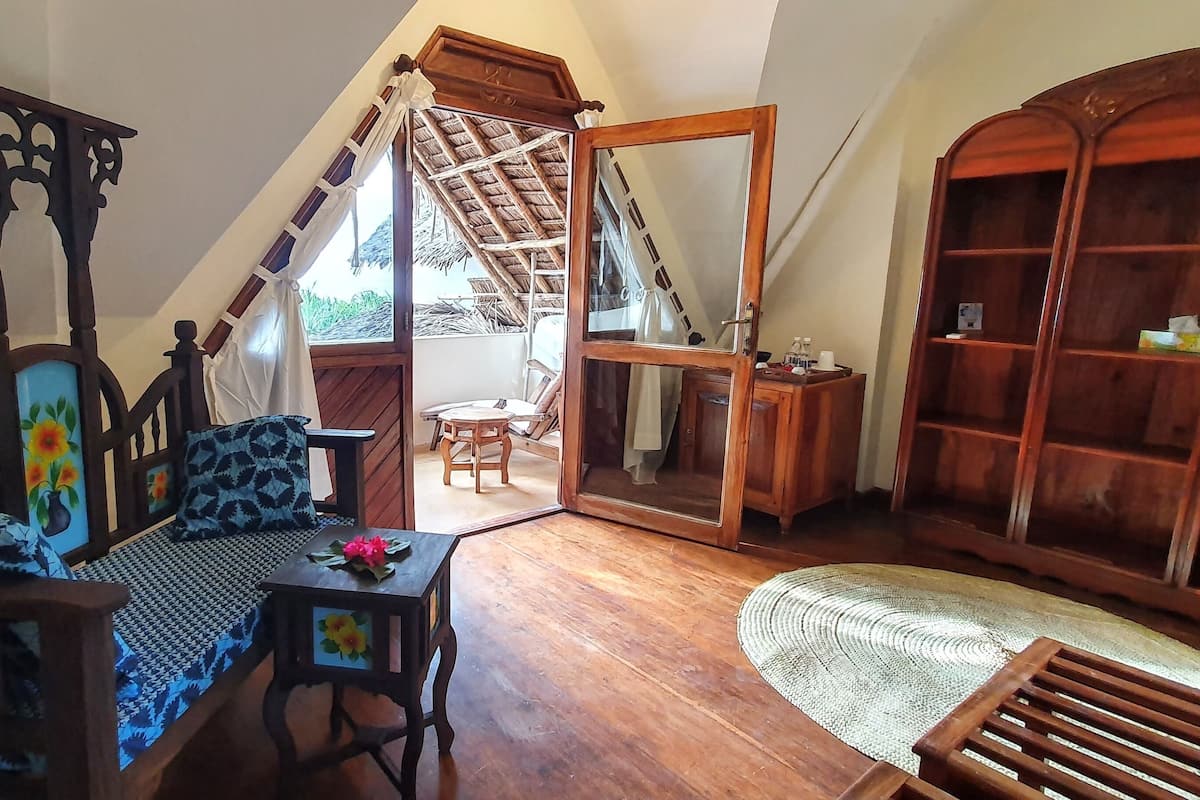 A room with a wooden bed, a wooden chair, a small table with a flower, a mirror, and a wooden cabinet.
