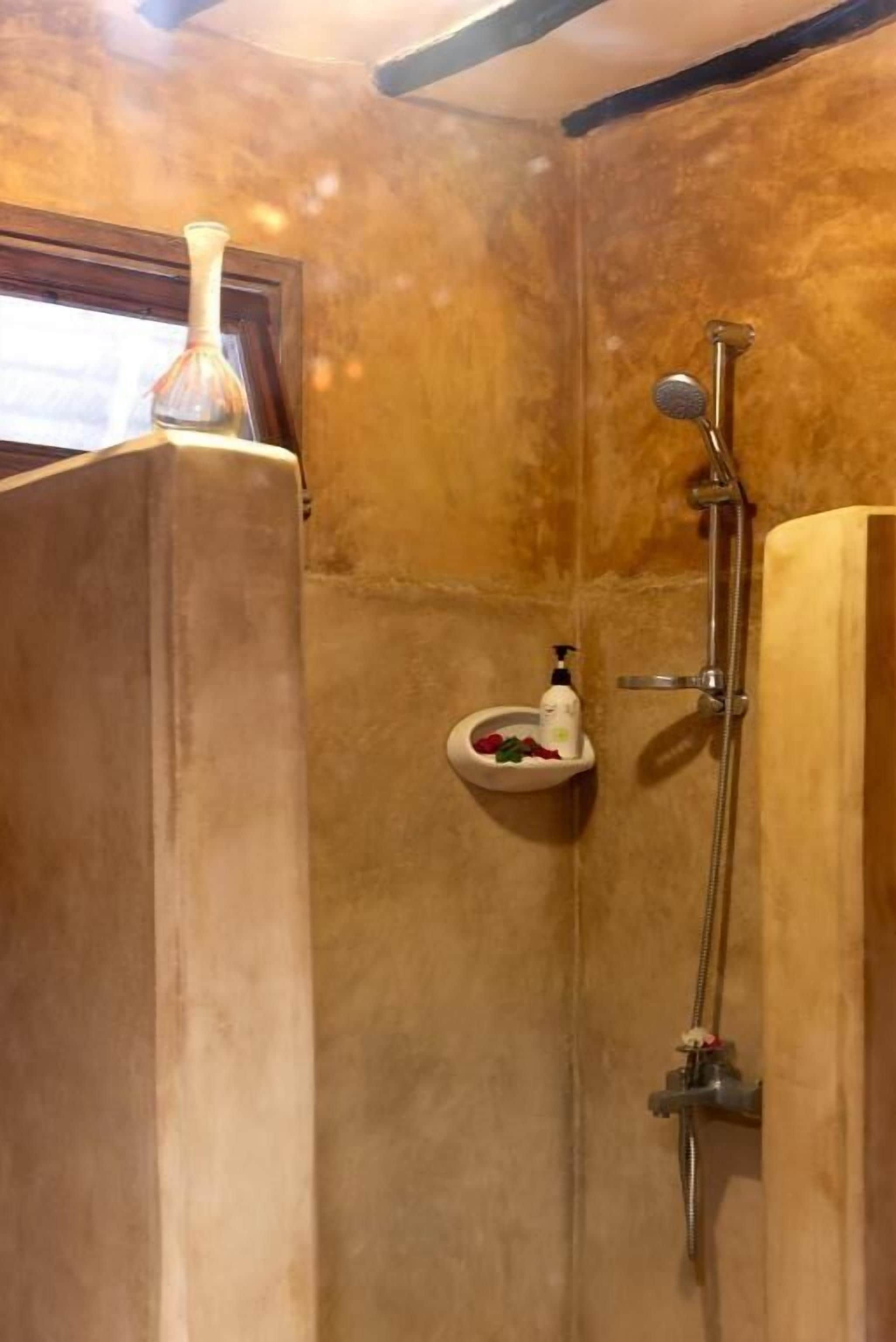 A bathroom with a wooden vanity, a shower with a handheld showerhead, and a soap dispenser on a small shelf.