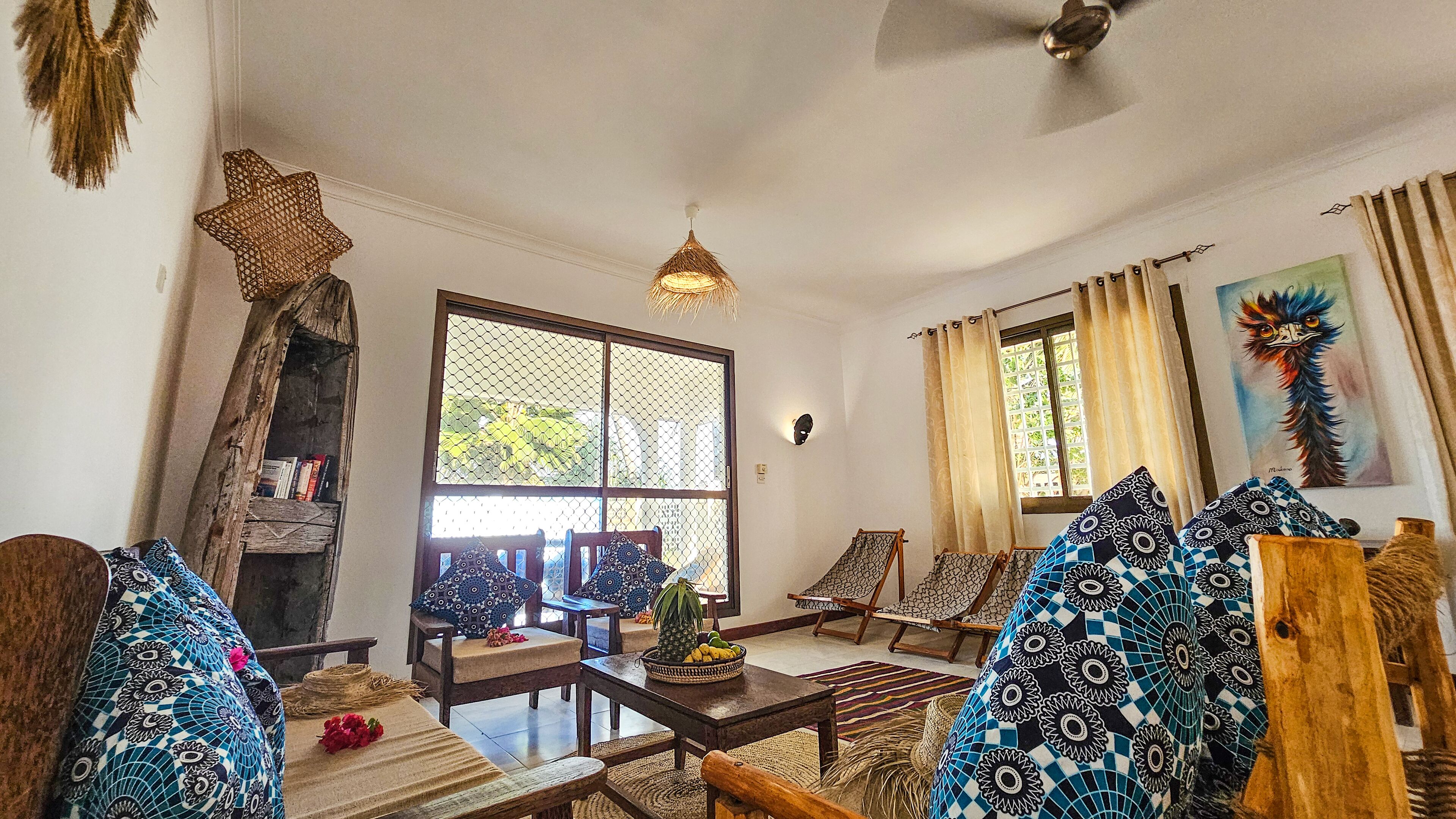 A cozy living room with a wooden coffee table, patterned cushions, and a large window with curtains.