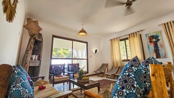 Una sala de estar acogedora con una mesa de centro de madera, cojines estampados y un amplio ventanal con cortinas.