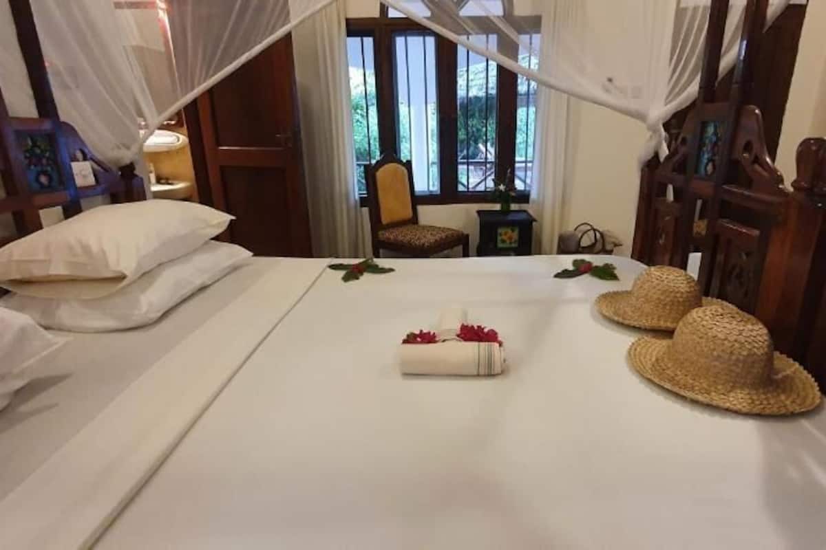 A hotel room with a bed, a chair, a window, and a bedside table.