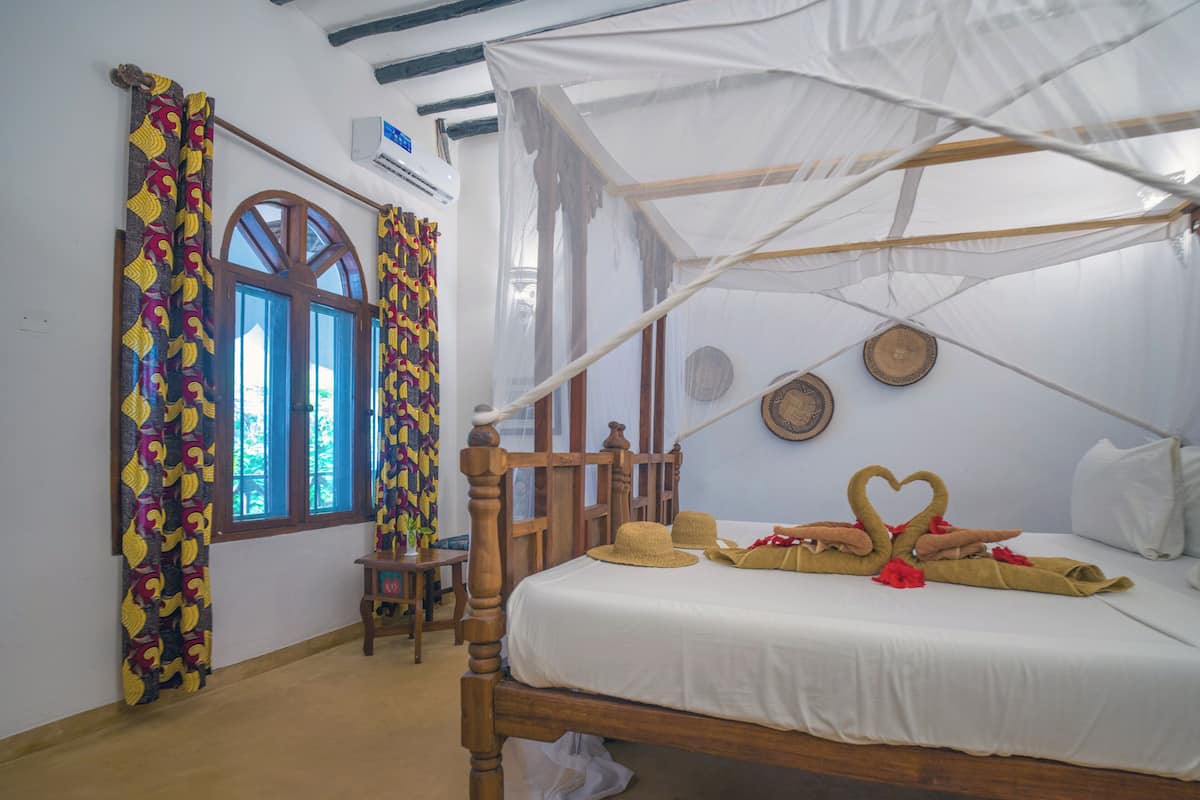 A room with a bed, a window, a chair, and a mosquito net.