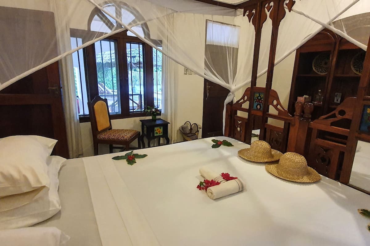 A bed with a canopy, a small table with a vase, and a chair.