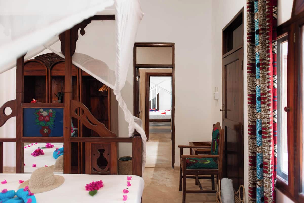 A room with a bed, a wooden chair, a mirror, and a window with curtains.
