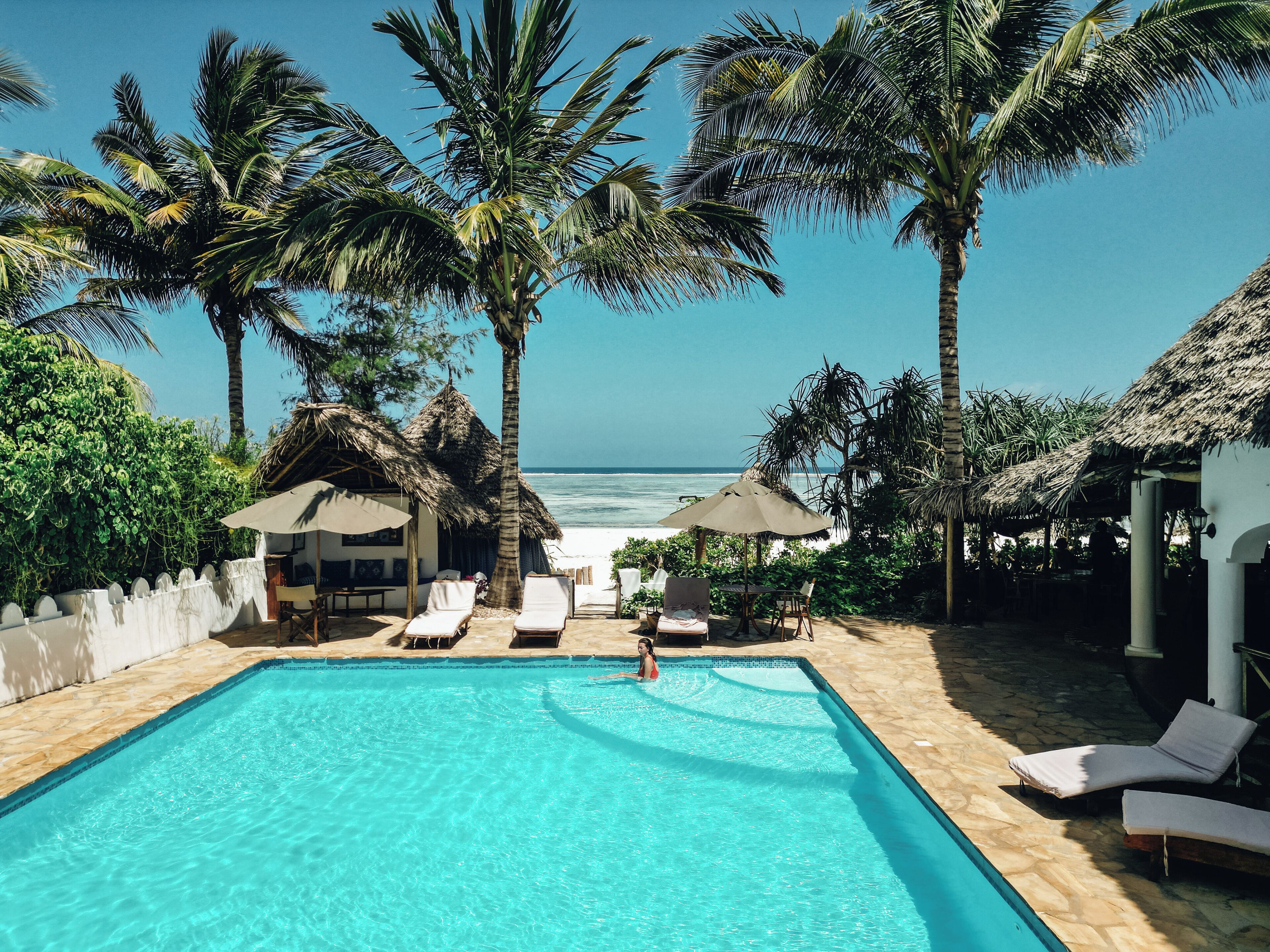 A pool area with lounge chairs, a thatched-roof structure, and a view of the ocean.