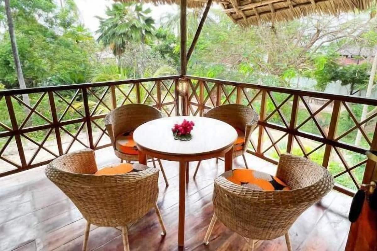 A wooden deck with a thatched roof, wicker chairs, and a round table with a flower centerpiece.