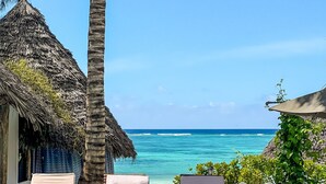 A poolside area with lounge chairs, a palm tree, and a view of the ocean. - Zoi Retreat Hotel Zanzibar (Matemwe)