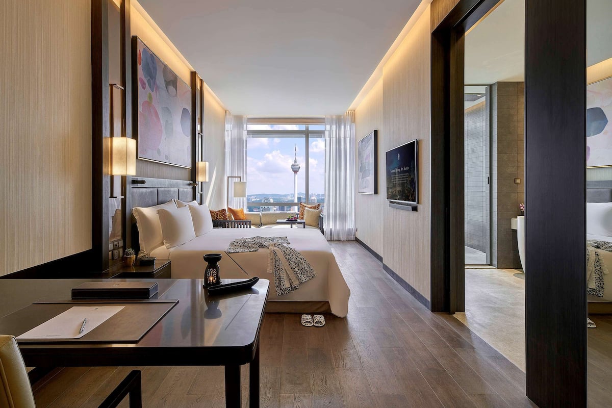 Habitación de hotel con una cama grande, un escritorio y vistas a la ciudad.