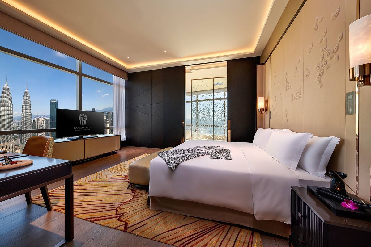 Habitación de hotel con una cama grande, un escritorio, un televisor y vista al horizonte de la ciudad.