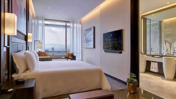 Een moderne hotelkamer met een groot bed, een bureau, een kaptafel met spiegel en uitzicht op de stad door grote ramen.