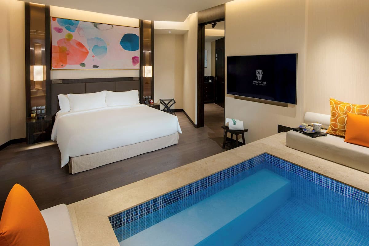 Una habitación de hotel con una cama grande, una zona de estar pequeña con televisión y una piscina.